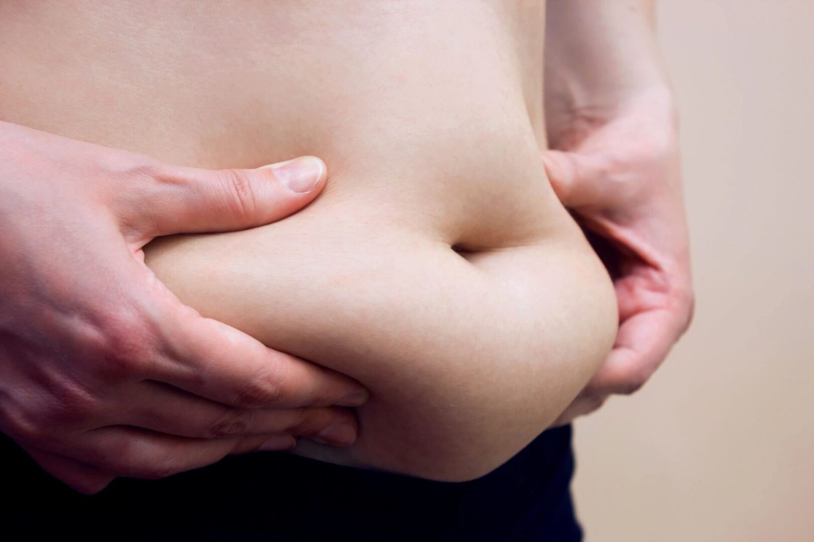 Person holding excess belly fat with both hands.