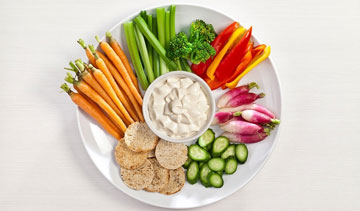 A colorful vegetable platter with dip and crackers.