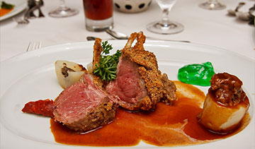 Gourmet lamb chops with sauce and artistic vegetable garnishes.