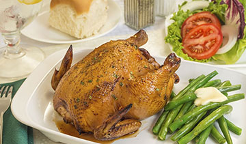 A roasted whole chicken served with green beans and tomato slices.