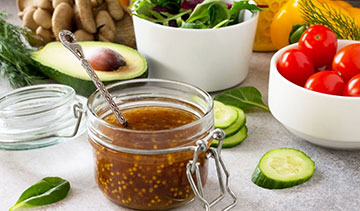 A jar of mustard sauce with a spoon and fresh vegetables around.
