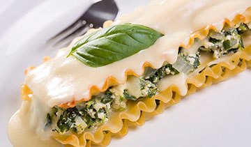 Close-up of creamy spinach and cheese lasagna with a basil leaf on top.