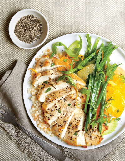 Grilled chicken with couscous, green beans, and citrus slices on a white plate.