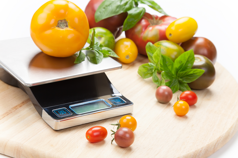 Variety of colorful tomatoes on a digital kitchen scale and wooden board.