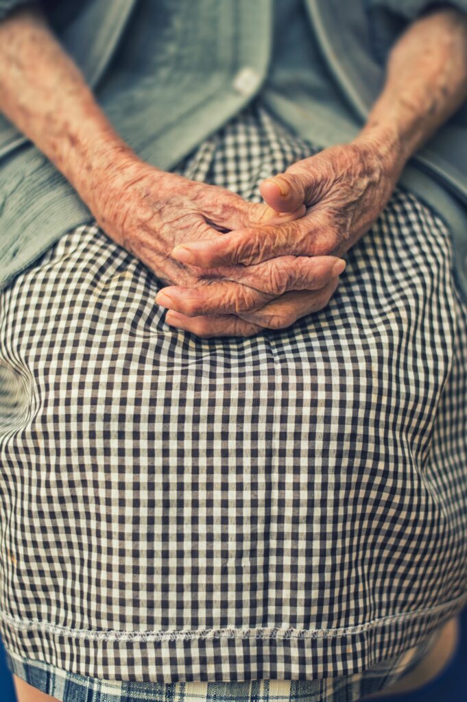 Elderly hands resting gently on a checkered dress.